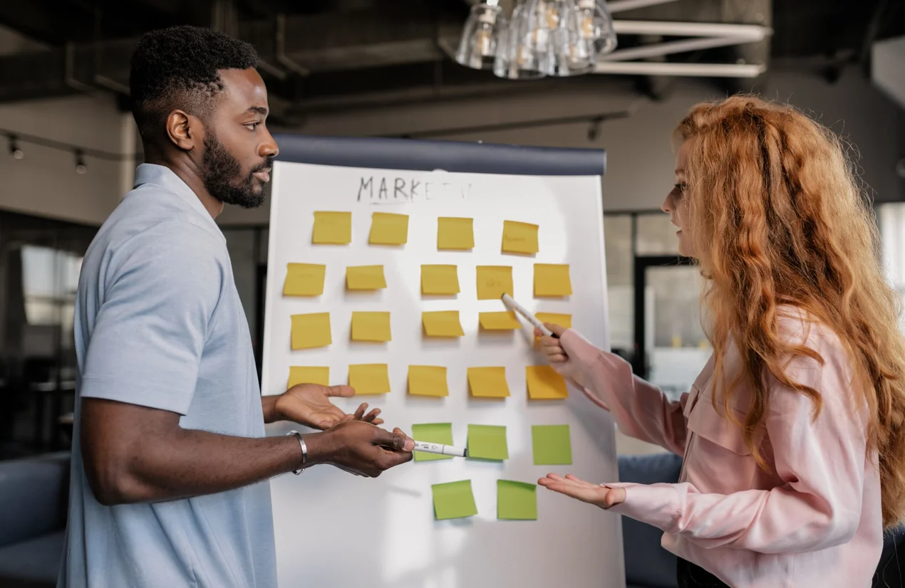 Deux personnes organisant des idées avec des post-it sur un tableau marketing